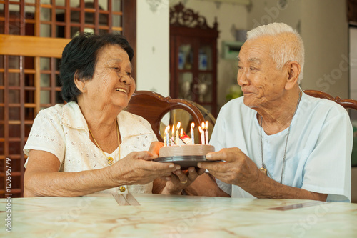 Asian senior couple holding a cake and smiling in living room