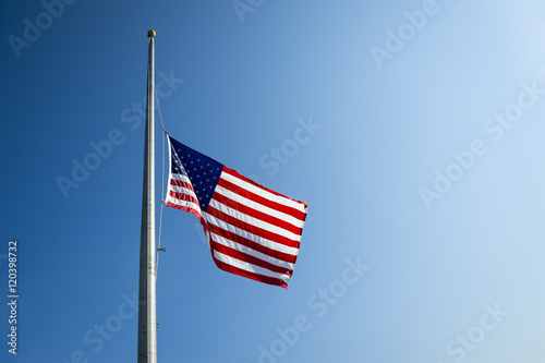 American flag flies at half mast backlit by the sun in bright blue sky photo