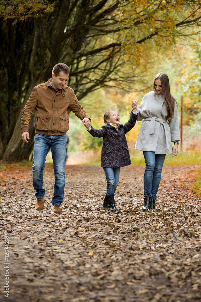 Lovely family walking in the autumn forest. Happy parents enjoying fresh air and beautiful nature, holding hands, talking, smiling and laughing. Healthy lifestyle
