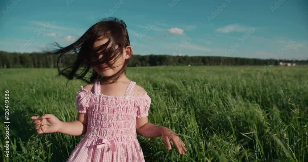 little Asian girl standing in a green field of young wheat, flowing hair,slow motion little Asian girl standing in a green field of young wheat, flowing hair,slow motion