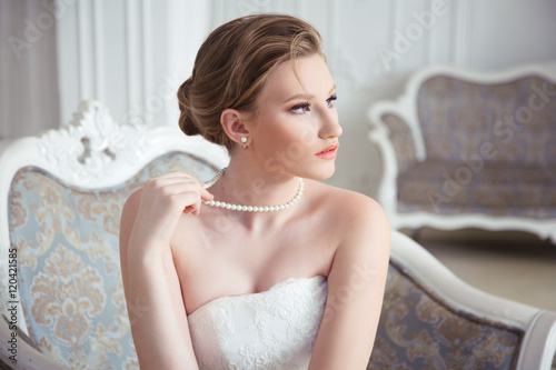 Portrait of charming bride holding in anticipation of a pearl necklace, in the interior.