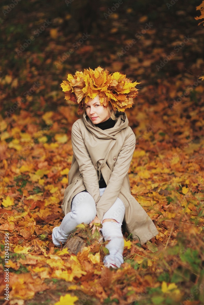 Young beautiful smiling girl with a crown of autumn maple leaves sitting on fallen leaves in the forest. Young beautiful smiling girl with a crown of autumn maple leaves sitting on fallen leaves in the forest.