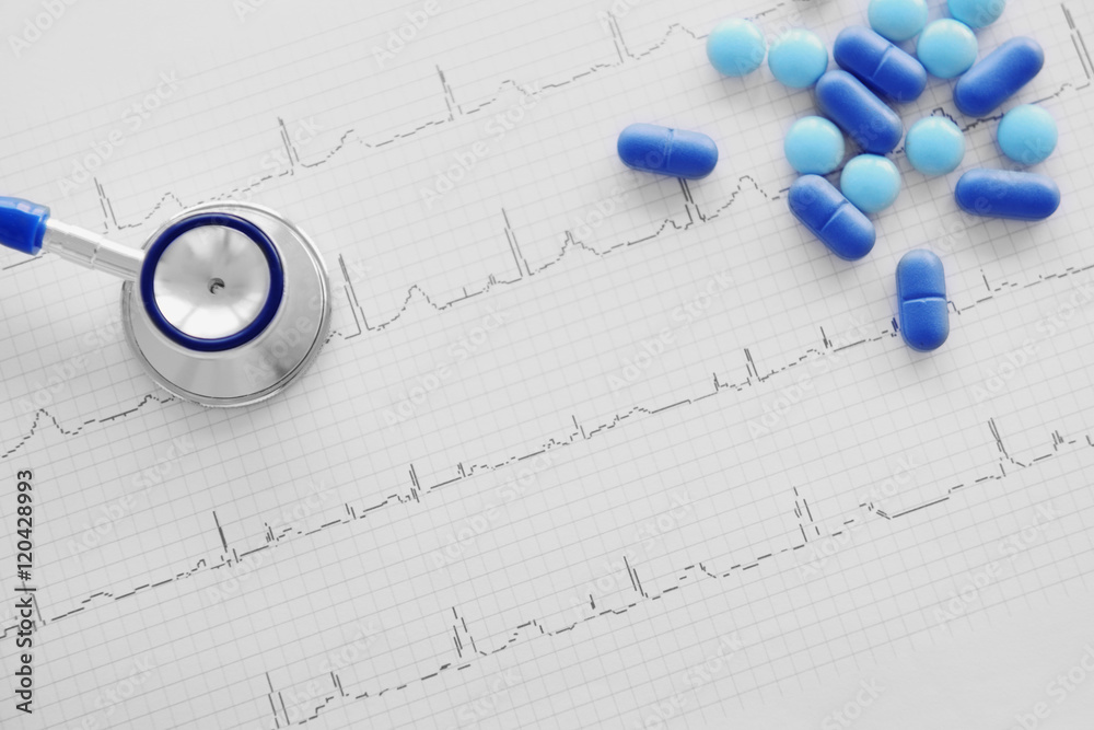 Stethoscope and pills on cardiogram, closeup