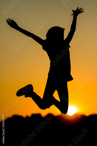 Dziewczynka skacząca z radości na tle zachodzącego słońca