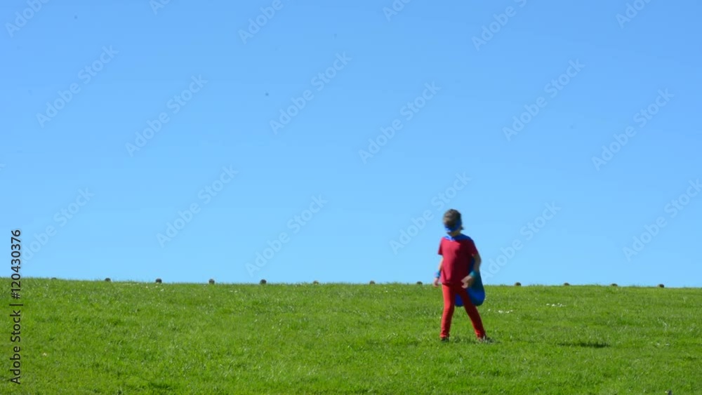 Superhero child (girl) runs in a green field against dramatic blue sky background with copy space. concept photo of Super hero, girl power, play pretend, childhood, imagination. Real people Superhero child (girl) runs in a green field against dramatic blue sky background with copy space. concept photo of Super hero, girl power, play pretend, childhood, imagination. Real people