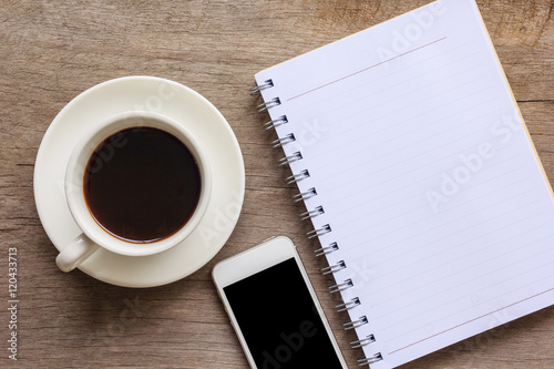 Top view and close up of old wooden desktop with notebook, smartphone and coffee cup. 