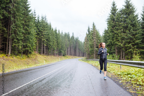Young slim woman jogging on road at rainy morning