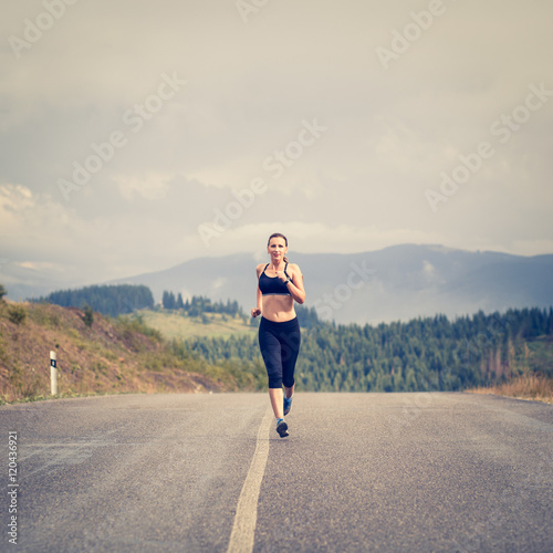 Young female runner on road cross in mountains