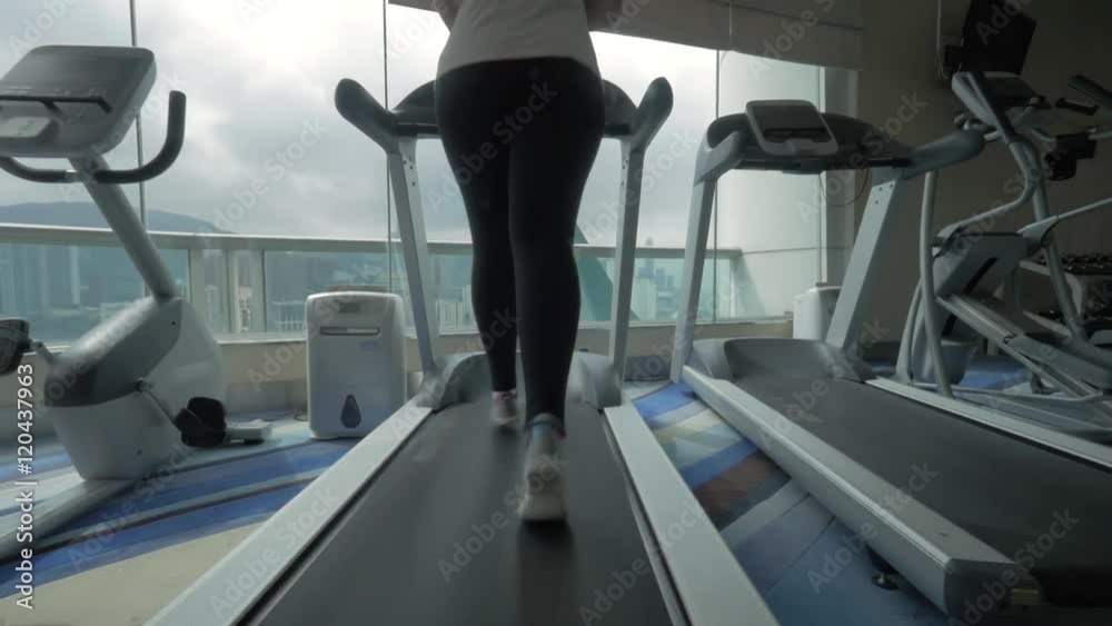 Young woman having workout on running machine in modern equipped gym with view to the Hong kong city