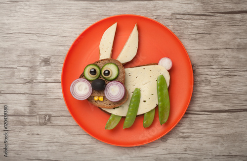 Funny rabbit made of bread and vegetables on orange plate