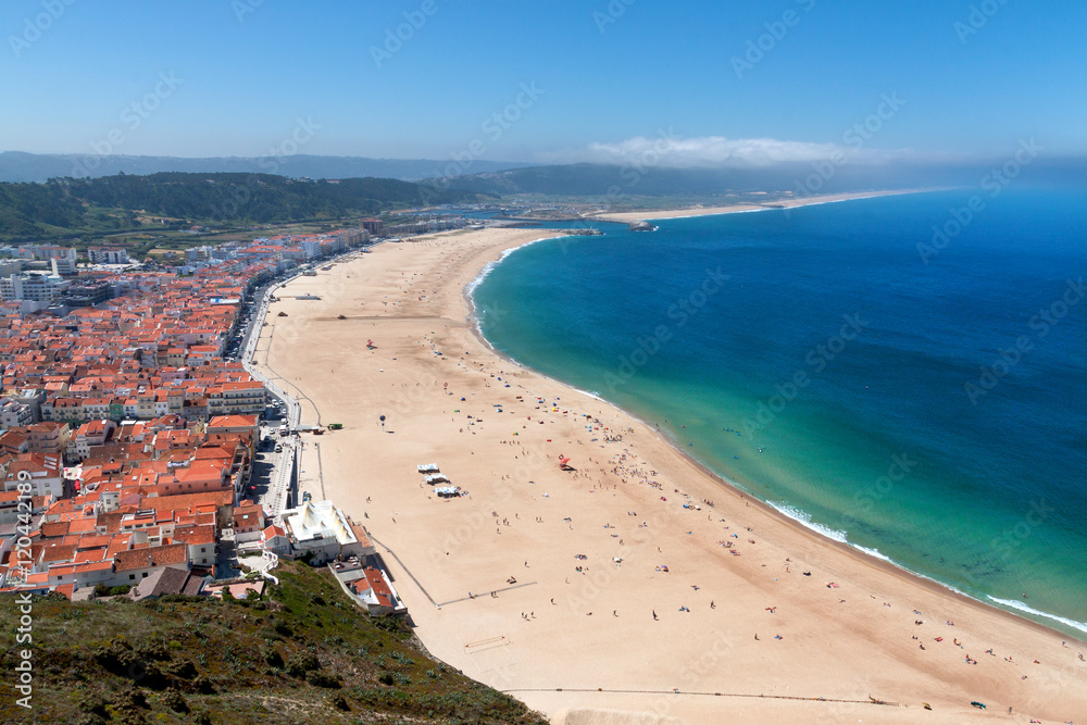 Fototapeta premium View over sandy beach coastline with ocean, sunlight, blue sky at Nazare, Portugal