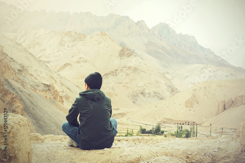 Young male traveler sitting on the sand cliff, thinking about something in Leh, Ladakh, India.