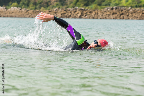 Swimmer. Man swimming Freestyle strokes in open water outdoor competition. Competitive triathlete male sport swimmer wearing swimming goggles, cap and wet suit taking air.