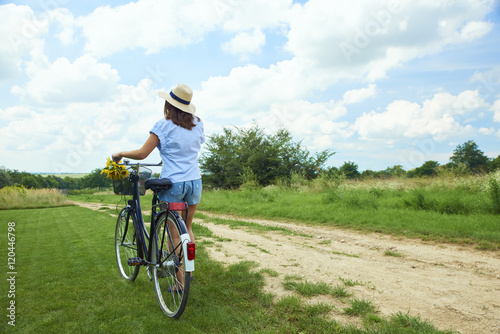 Fototapeta Naklejka Na Ścianę i Meble -  Relaxing outdoor. Young woman riding bike through a field. Rear view.
