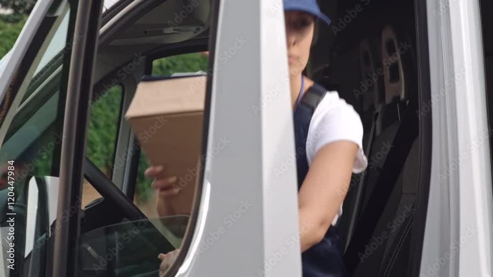 Delivery woman in blue uniform getting out from van, signing application form and walking with package to the house of client Delivery woman in blue uniform getting out from van, signing application form and walking with package to the house of client