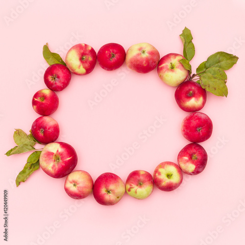 Top view on delicious red organic apples with leaves in a shape of circle on light pink background. Healthy food concept