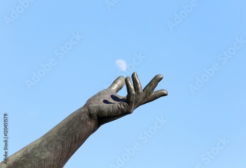 hand of statue trying to catch the moon in the sky