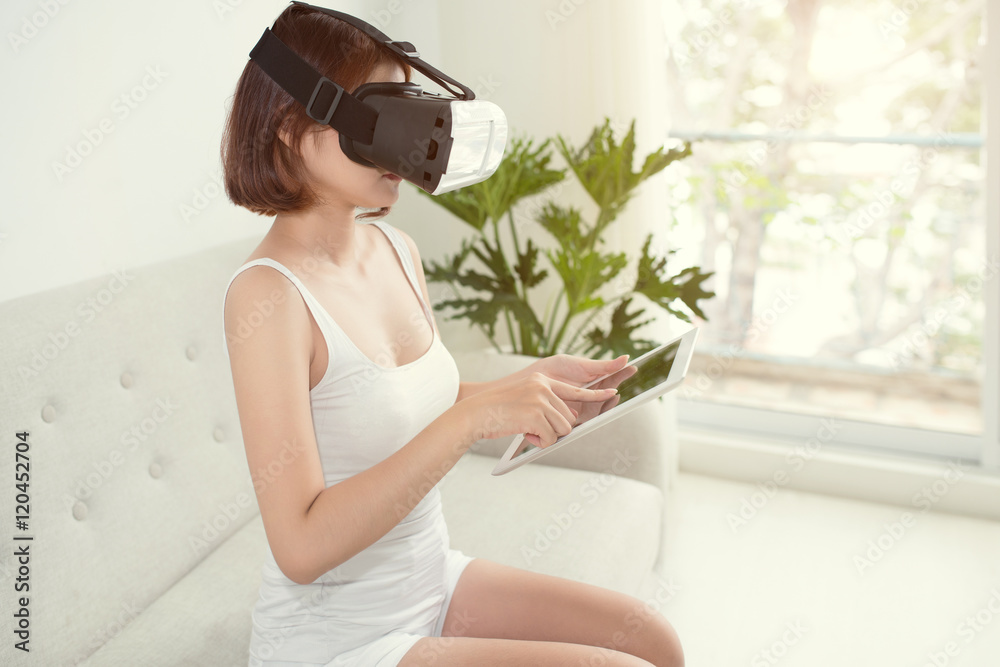 Young Woman Using VR Goggles and Touching Tablet at Home. Young Woman Using VR Goggles and Touching Tablet at Home.