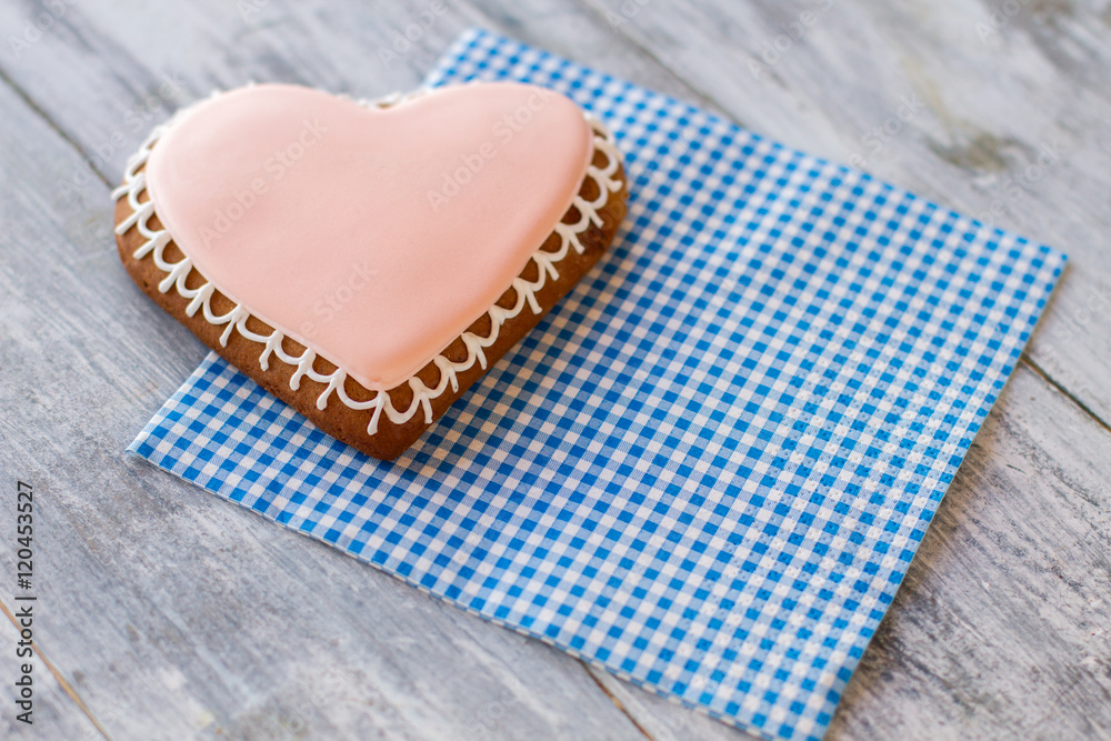 Obraz premium Heart-shaped biscuit on napkin. Pastry with light pink frosting. Sweet symbol of love. Live in joy.