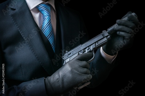 Mafia man or racketeer holds pistol with silincer in hands. Low key photo.