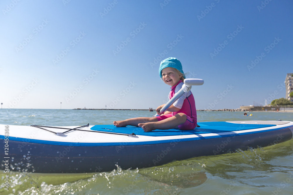 Obraz premium Kleines Mädchen sitzt auf dem Surfbrett im Meer