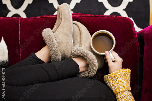 Low section of woman wearing fur slippers, holding coffee cup