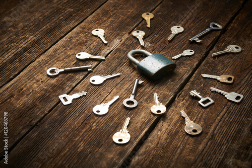 A lot of metal keys and a steel lock on a wooden boards