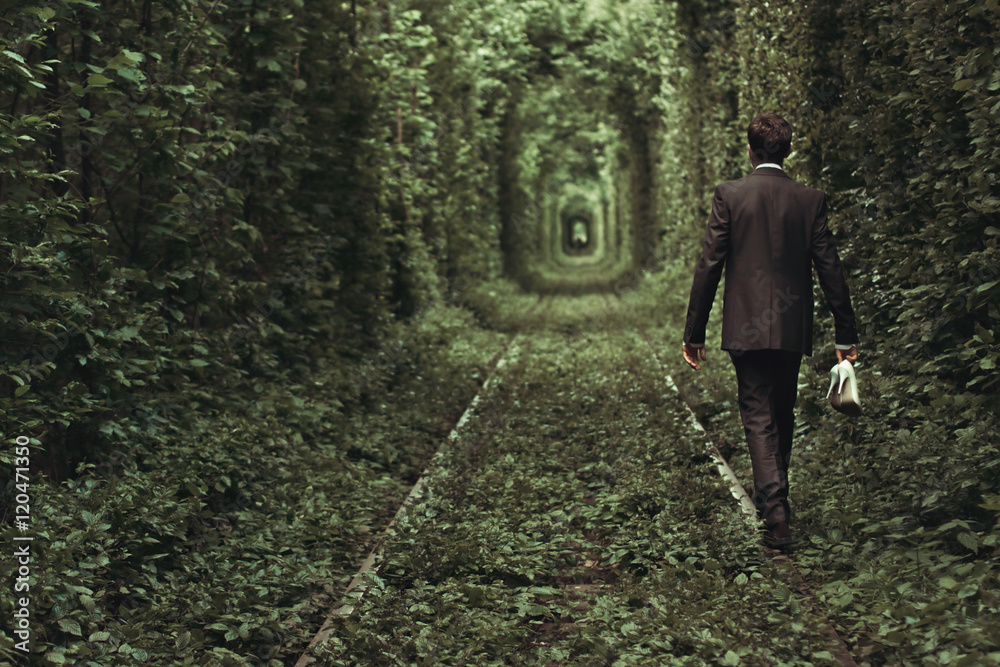 elegant groom walking with shoes in his hand  in tunnel formed b