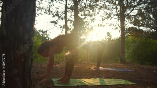 Girls practicing yoga stretching at sunset in forest Padahastasana Slow motion photo