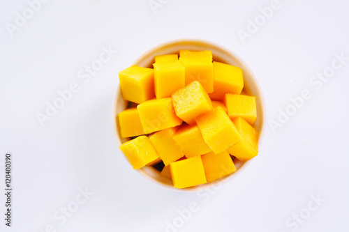 Top view of diced ripe mango cube in a white bowl on a white background. 