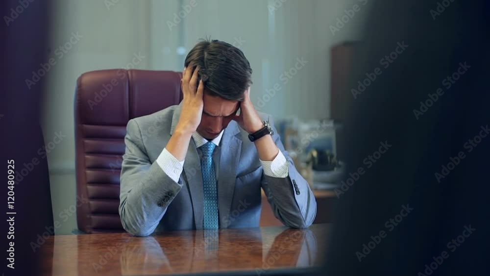 Disappointed tired young businessman sitting at his desk with his head resting on his hands and eyes closed Disappointed tired young businessman sitting at his desk with his head resting on his hands and eyes closed