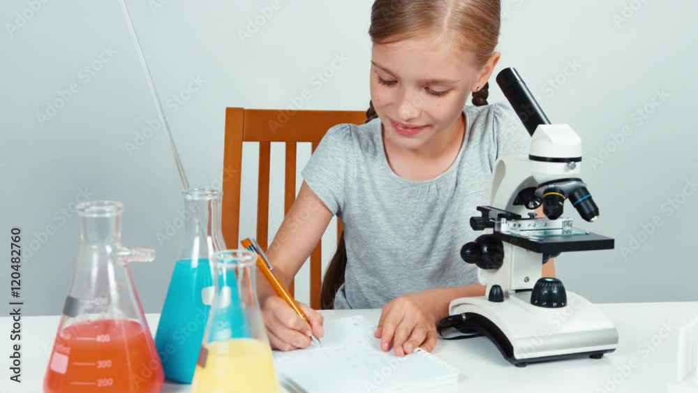 School girl using microscope and something writing in her exercise book. Isolated on white. Panning School girl using microscope and something writing in her exercise book. Isolated on white. Panning