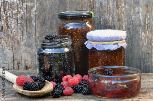 mûres et framboises et confiture en bocaux  sur fond bois  photo