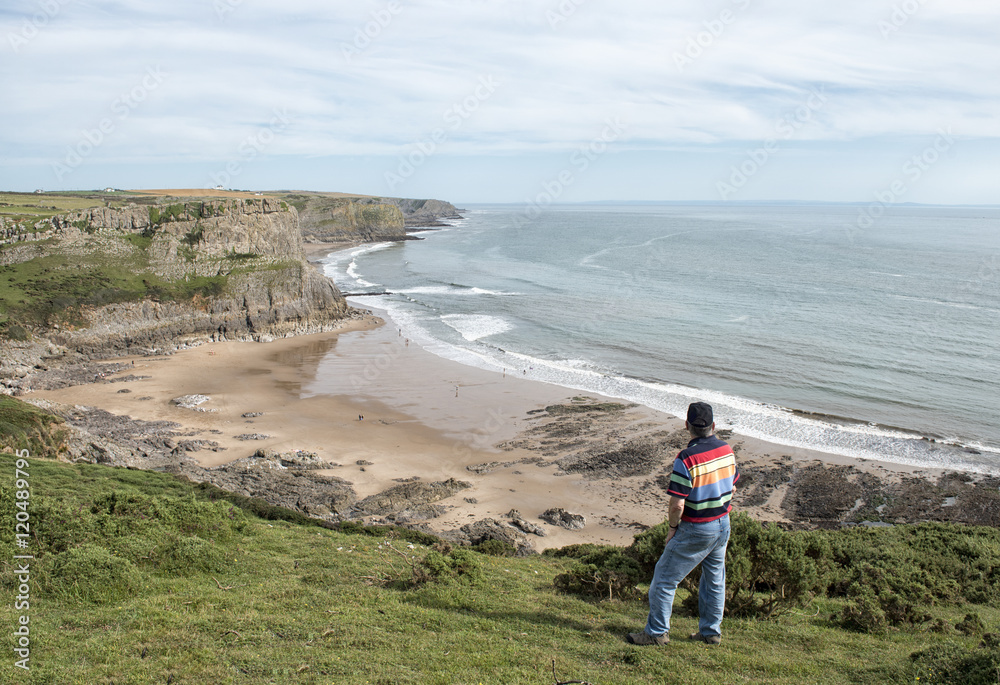 Landscape image of a mature man looking over a beach in the Gower Peninsula. 