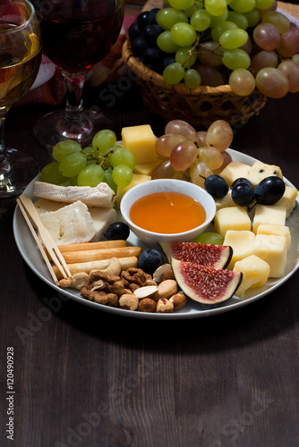 plate of cheeses, snacks, fruits and wine on a dark background