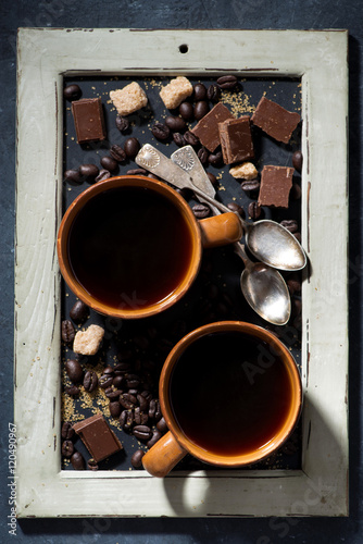 two cups of black coffee, sugar and chocolate on a blackboard