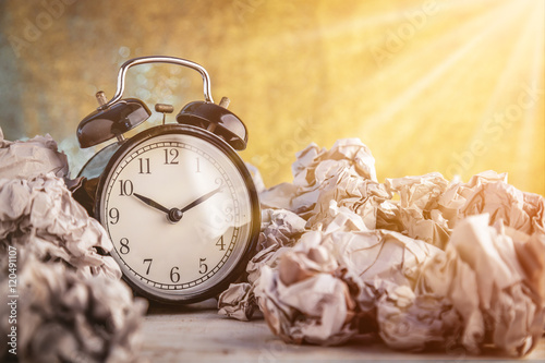 Alarm clock in a wastepaper concept for a time waste of time with golden bokeh blur texture background