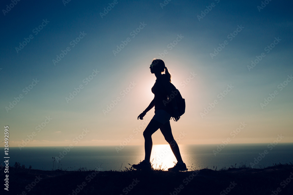 silhouette Young woman tourist with backpack goes on the background on sunset sky and sea.