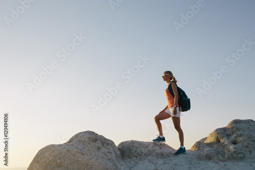 Young woman hiker with backpack standing on cliff and looking forward. lady tourist on top of a mountain enjoying view before sunset. Sport lifestyle travel concept © skvalval