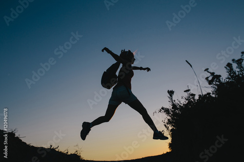 silhouette young woman tourist with backpack jumping through the gap between hill. Woman jumping over a ravine