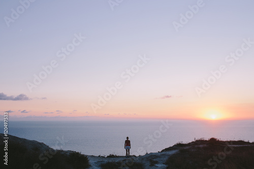 Young woman hiker standing on hill and looking to forward at sea. back view