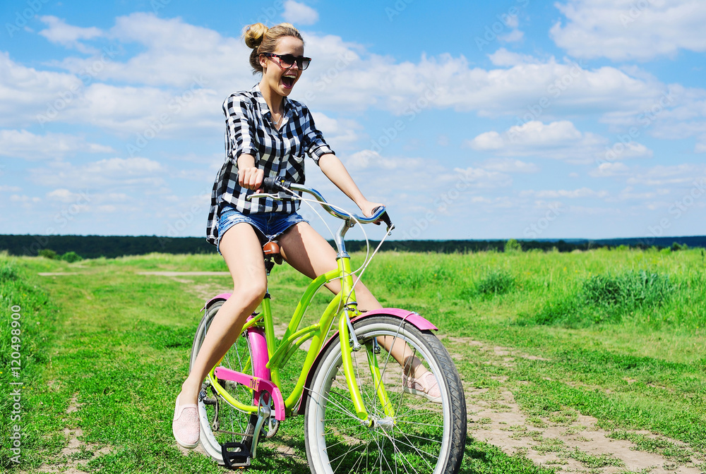 Beautiful girl riding bicycle outdoors across the green sunny field