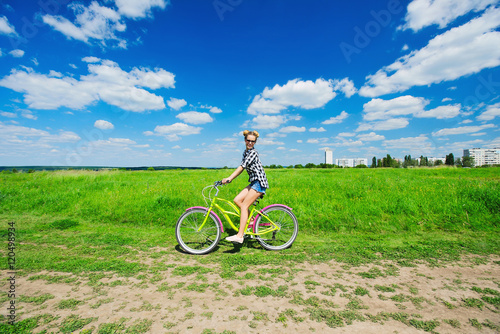 Beautiful girl riding bicycle outdoors across the green sunny field