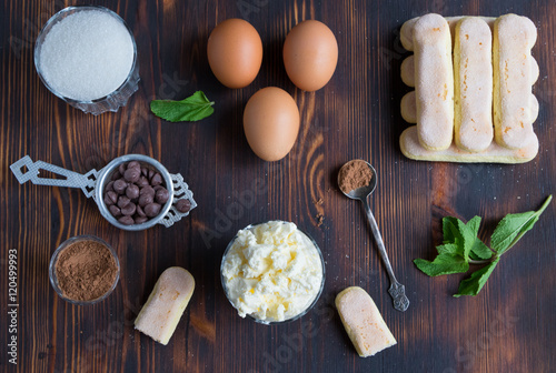 Ingredients of traditional italian dessert tiramisu - ladyfingers cake, eggs, sugar, mascarpone creme, cocoa, chocolate and peppermint on wooden background, top 