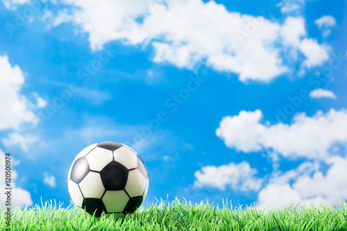 toy football  soccer  on fake green grass against clouds and blue sky