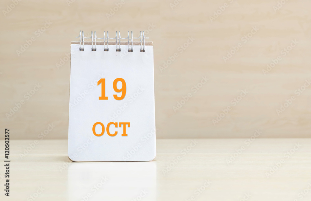 Closeup surface note book with orange 19 oct word in page on blurred brown wood desk and wood wall textured background with copy space under window light Closeup surface note book with orange 19 oct word in page on blurred brown wood desk and wood wall textured background with copy space under window light