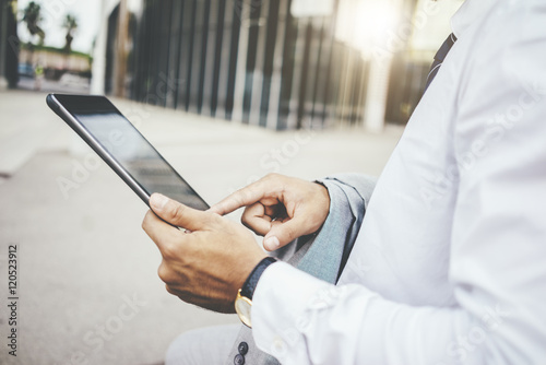 Close-up of male hands using digital tablet outside, businessman holding tablet pc and searching information in internet, focus on hands, flare light