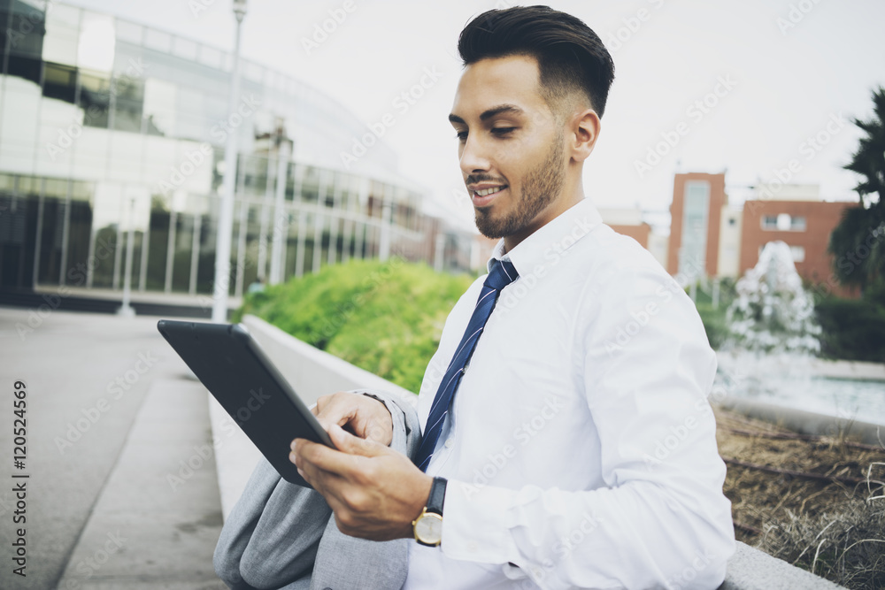 Young happy smiling businessman using modern digital tablet outside, professional male latin lawyer reading information via portable tablet Young happy smiling businessman using modern digital tablet outside, professional male latin lawyer reading information via portable tablet