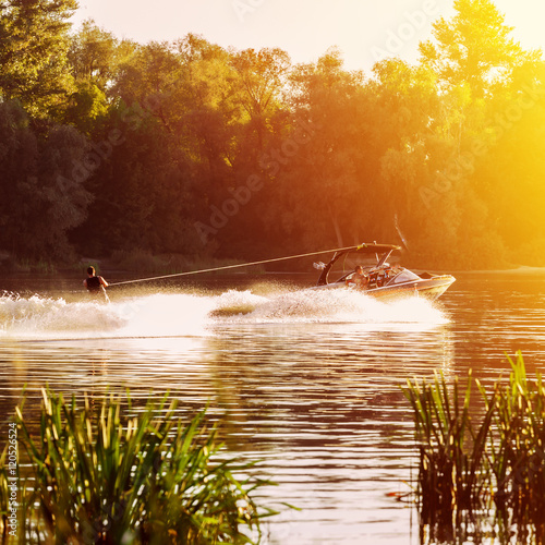 boat pulls man water skiing on the river. Sunset. Splashes of water.