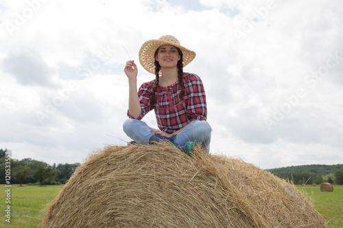Beautiful brunette woman sitting on hay bale in warm summer day